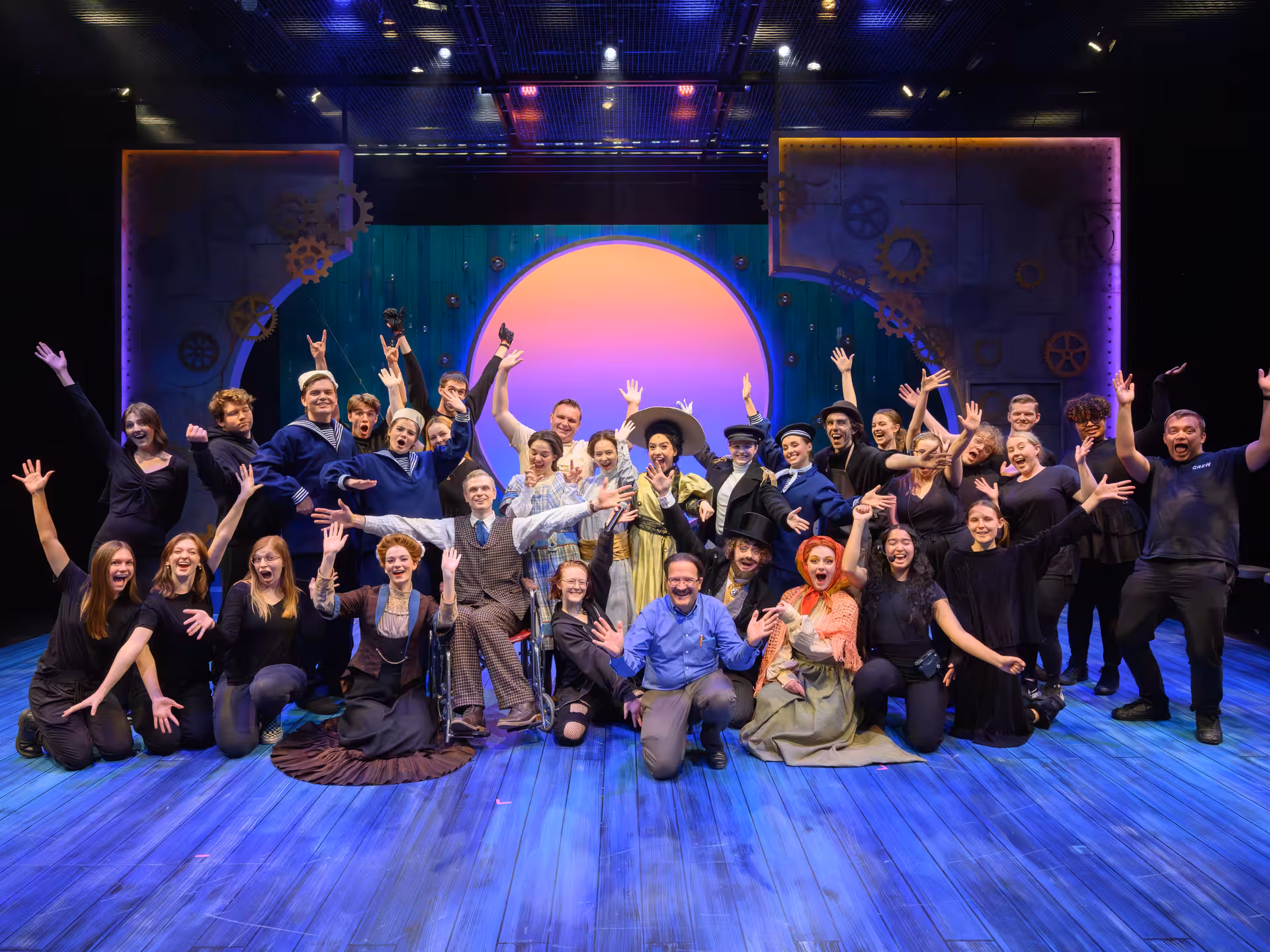 The cast and crew of Ozma of Oz energetically poses on set smiling wide with their arms in the air
